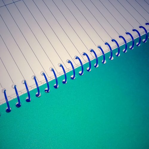 dandex 内容编辑伏案写作，桌上摊开多份标注了日期的打印资料，屏幕显示正在比对的两个页面，呈现逐条核实的工作状态